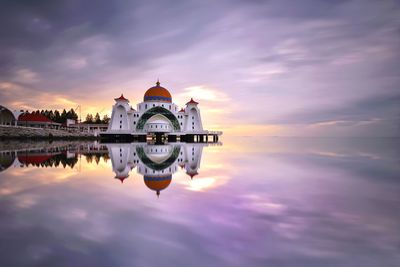 Reflection of mosque in sea against sky during sunset