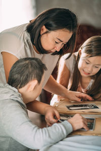 Young asian woman with a girl and elderly woman with down syndrome looks at photos in  album. memory