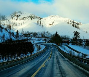 Country road passing through snow covered mountains against cloudy sky