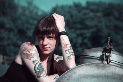 Portrait of young tattooed woman with hand in hair leaning on metal