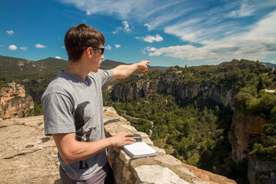 Young man standing on cliff against sky