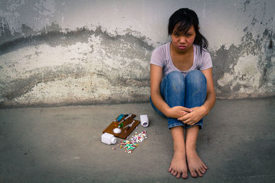 Depressed teenage girl sitting by narcotics against wall