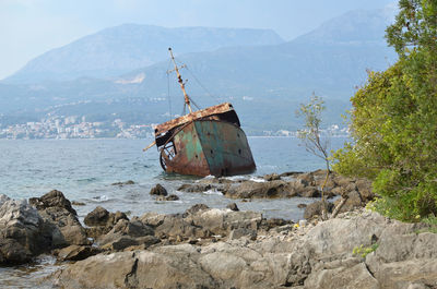 Abandoned ship in sea against mountains