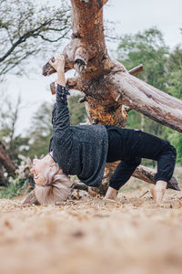 Full length of woman hanging on fallen tree at forest