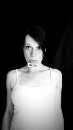 Portrait of young woman standing against black background