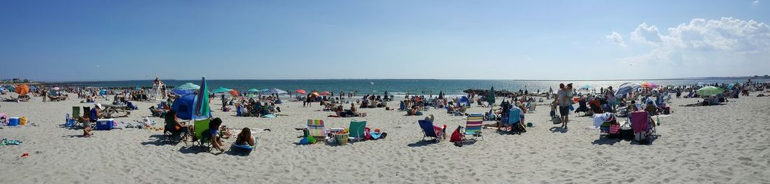 Panoramic view of people at beach against sky on sunny day