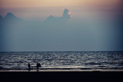 Silhouette people standing on beach against clear sky during sunset