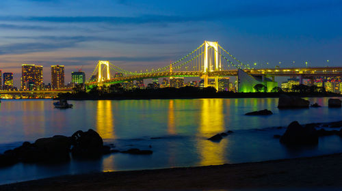 Illuminated bridge over river with city in background