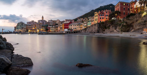 Buildings by river against cloudy sky