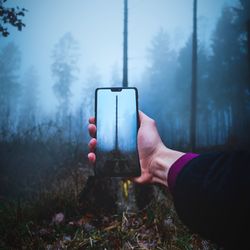 Midsection of man using mobile phone against trees