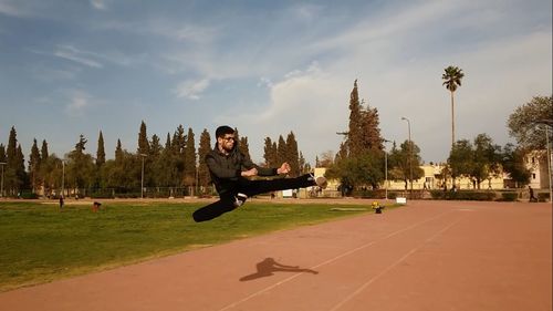 Man practicing karate kicking in mid-air against sky