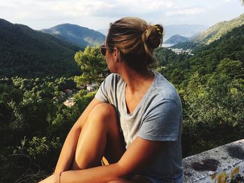 Mid adult woman sitting on wall by mountains