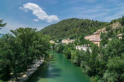 Scenic view of river amidst trees and buildings against sky