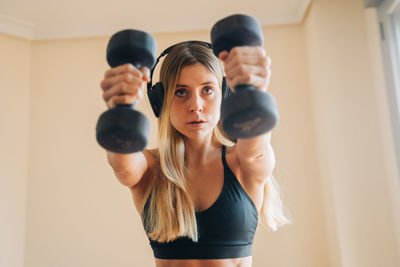 Determined female in sportswear with headphones listening to music while doing lunges exercise with weight at home