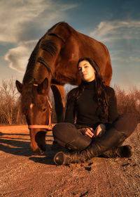 Young woman sitting on field against sky