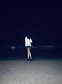 Rear view of woman standing at beach during night