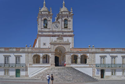 People outside temple against clear blue sky