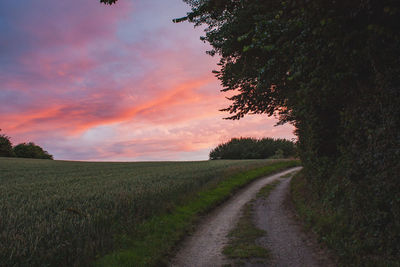 Road amidst field against sky during sunset