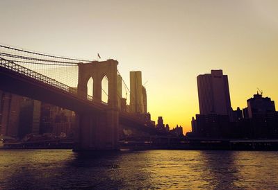 Low angle view of brooklyn bridge over river against clear sky during sunset in city