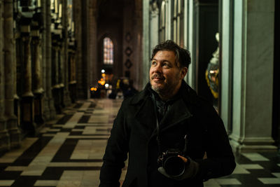 Portrait of smiling man standing in corridor with a analog camera