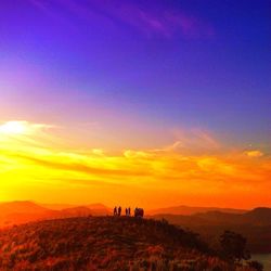 Silhouette of people on landscape against sunset sky