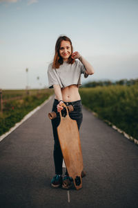 Portrait of young smiling woman holding skateboard on road