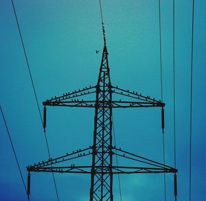 Low angle view of electricity pylon against clear blue sky