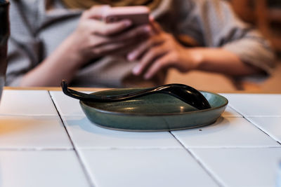 Close-up of spoon in plate against woman in background