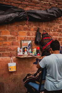 Rear view of man sitting on table against brick wall