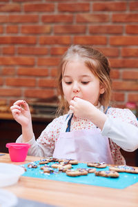 Cute girl tasting cookie on table in workshop