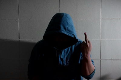 Man wearing hood gesturing standing against wall
