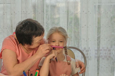 Grandmother making mustache of granddaughter