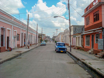 Cars on road by buildings in city against sky