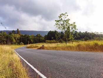 Empty road by trees against sky