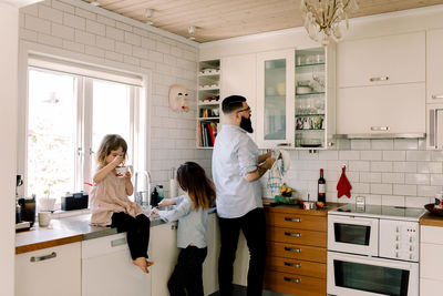 Father and daughter working at counter while girl eating food in kitchen