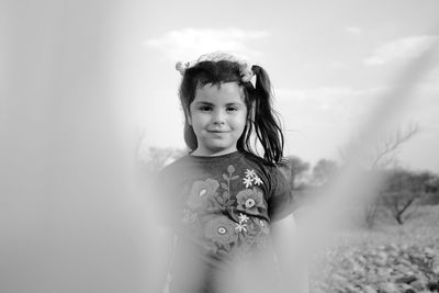 Portrait of cute girl standing on field against sky