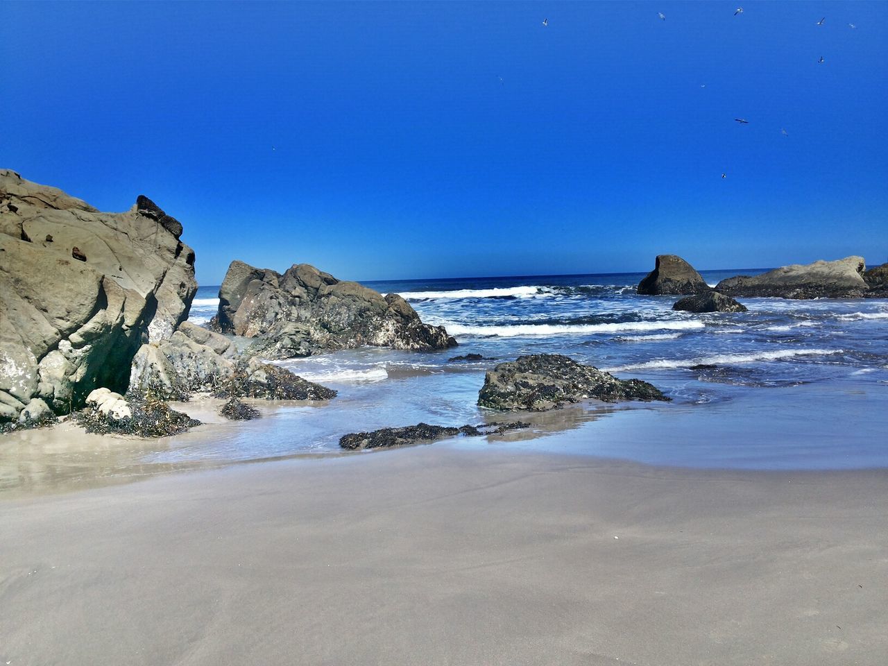 sea, clear sky, beach, water, blue, copy space, tranquil scene, shore, scenics, tranquility, sand, horizon over water, beauty in nature, nature, rock formation, rock - object, wave, coastline, surf, idyllic