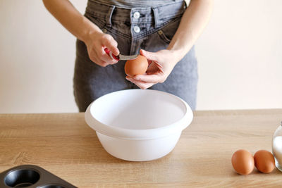 Woman breaks an egg with a knife over a plate to cook a delicious meal