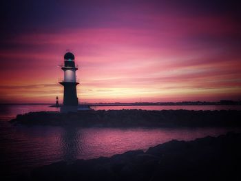 Lighthouse by sea against sky during sunset