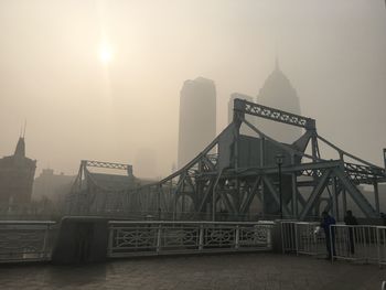 Bridge against buildings during foggy weather on sunny day