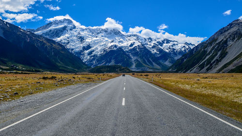 Street leading towards snow covered mountains against sky