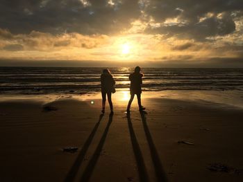 Silhouette friends standing on beach against sky during sunset