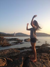 Woman standing on rock at beach against sky