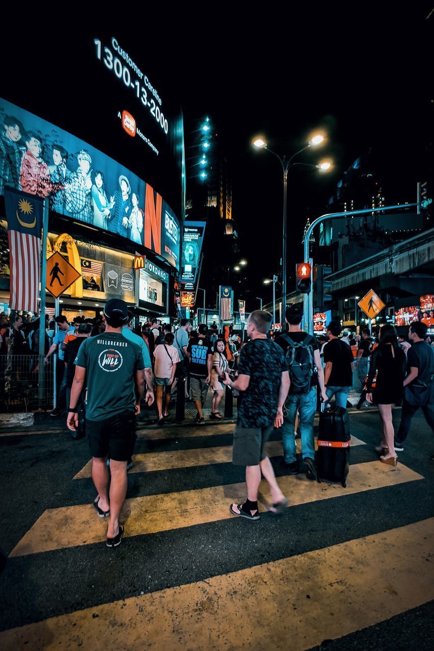 PEOPLE WALKING ON ILLUMINATED STREET IN CITY AT NIGHT