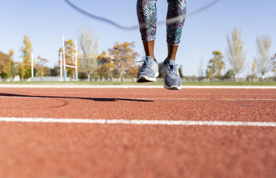 Female athlete jumping with jump rope over sports track on sunny day