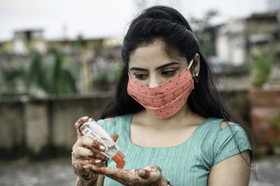 Close-up of woman wearing red mask using hand sanitizer