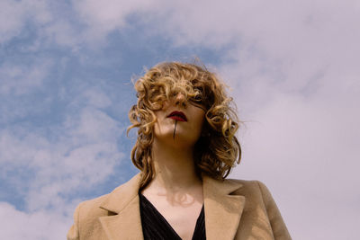 Low angle portrait of woman standing against cloudy sky