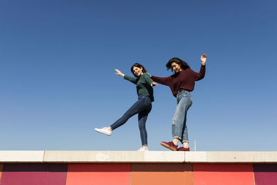 Low angle view of people jumping against clear blue sky