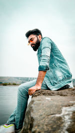 Young man on rock against sky