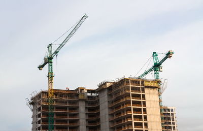 Low angle view of crane by building against sky